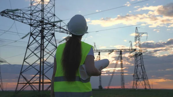 An electrician on the background of high towers of power plants looks at the project for the development of an electrical structure, the expansion of the electrical voltage of volts in the wires