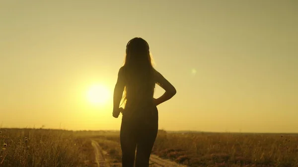 Chica feliz corre para cumplir su sueño al atardecer, haciendo deportes trotando al amanecer, escuchando música en una mañana activa trotar en rayos de luz solar, cuidando de su salud y estar en forma, figura humana —  Fotos de Stock