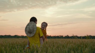 Gün batımında buğdaylı bir tarlada çocuğu olan nazik bir çiftçi anne, ekmek yapmak için tahıl yetiştiriyor, mutlu bir çocuk, bir çiftlikte aile işi, kollarında bebekle büyüyen ekinleri inceliyor.