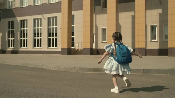 Bambino della scuola elementare è in esecuzione intorno al cortile della scuola con lo zaino sulle spalle, bambino piccolo è studente di prima elementare, curriculum moderno, un bambino attivo sulla strada, il desiderio di essere intelligente, ragazza felice — Foto Stock