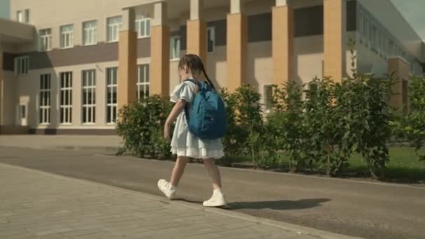 Niño de la escuela primaria está corriendo por el patio de la escuela con la mochila en los hombros, niño pequeño es estudiante de primer grado, plan de estudios moderno, un niño activo en la calle, el deseo de ser inteligente, chica feliz — Vídeo de stock