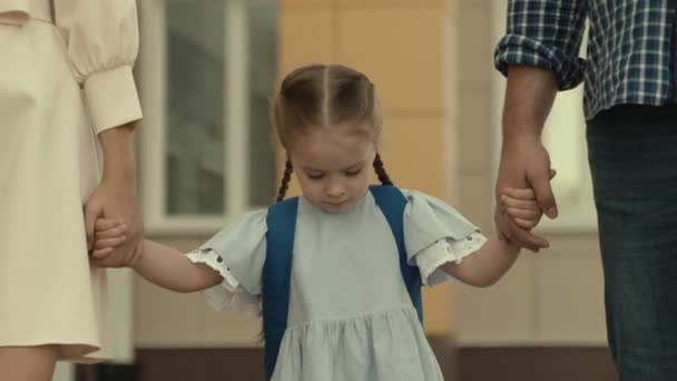 Niña va de la mano con los padres a la escuela, niño con una mochila en la espalda, la enseñanza en la escuela primaria, la enseñanza de los conocimientos del programa educativo de la escuela, la familia feliz — Vídeos de Stock