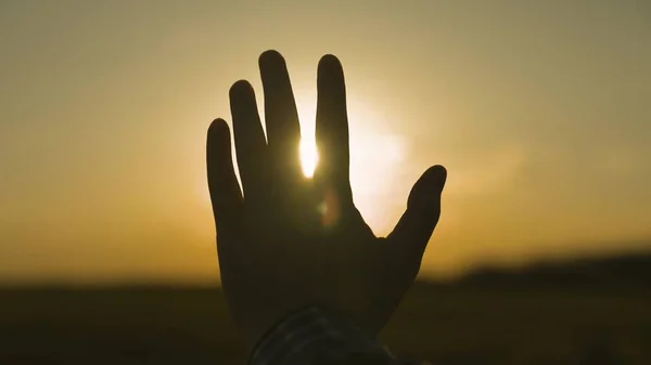 Silhouet van een menselijke hand bij zonsondergang, vragen de hemel om hulp, geloven in een droom, de schittering van de zon aan de hemel, een wandeling en 's avonds rust in een toeristische reis, bidden tot God — Stockfoto