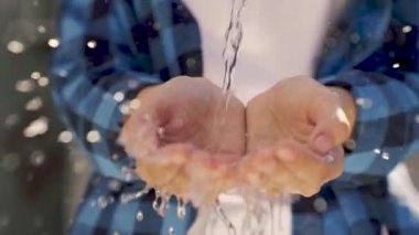 Bir insanın ellerine dökülen su damlaları, güneşin yansıtıcı parıltısında palmiyeleri yıkamak, havada uçan ıslak damlalar, suyun altında fırçalar, yavaş çekim.