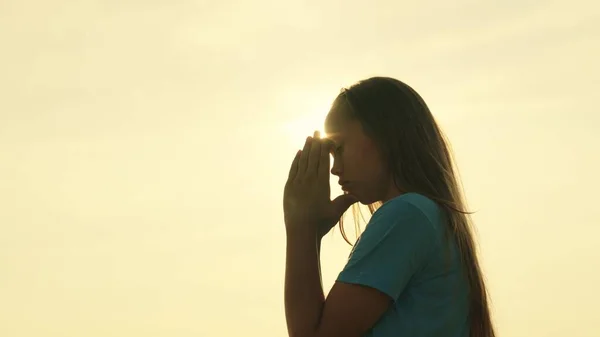A girl prays at sunset, be a religious person, believe in kindness, a childhood dream, pray looking at the sky in the glare, the inspiring mystery of a childs spiritual emotion, meditation at dawn