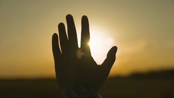 Egy emberi kéz sziluettje naplementekor, segítséget kérve az égtől, hinni egy álomban, a nap ragyogásában az égen, egy séta és esti pihenés egy turista utazáson, imádkozva Istenhez — Stock Fotó
