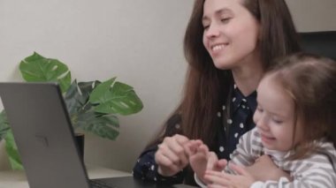 Evde dizüstü bilgisayarda çalışan serbest çalışan bir iş kadını kucağında küçük bir çocukla bilgisayar klavyesine mesaj yazıyor ve monitör ekranına bakıyor, çocuk annesinin kucağına oturuyor ve gülüyor.