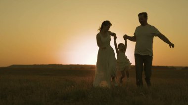 Mutlu aile gün batımında gökyüzünde koşar, anne ve baba aktif atlayışlarda çocukla oynar, anne ve babayla birlikte olmanın çocukluk hayali, anne ve babayla dışarıda eğlenmek, yavaş çekim, hayat değerleri kavramı