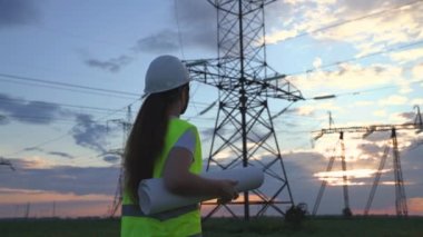 Yüksek elektrik santrallerinin arka planında bir elektrikçi elektrik yapısının geliştirilmesi projesine bakıyor, kablolardaki elektrik voltajının genişletilmesi