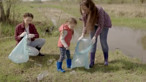 Un niño pequeño recoge basura en un equipo de voluntarios, una familia feliz, limpiando la ecología de la tierra de la basura, un ecosistema, manteniendo limpios los lugares de descanso, el niño con su madre limpia — Vídeos de Stock