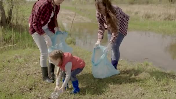 Voluntarios familia feliz recoge basura de plástico en bolsas, trabajo en equipo, niña ayuda a los adultos en la lucha por la protección del medio ambiente, eco, niño con mamá limpia la tierra del vertedero, trabajo de caridad — Vídeos de Stock