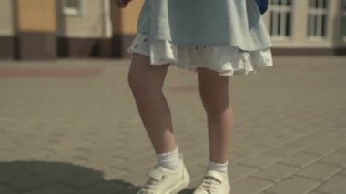 Küçük bir kız okul yolunda sırt çantasıyla yürüyor, spor ayakkabıları ayaklarının üzerinde, okul gününden sonra aktif bir çocuk, bir anaokulunda ilkokul eğitimi alıyor, çocukluk hayalleri kuruyor.