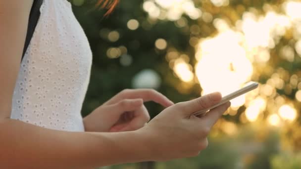 Una joven sostiene en su mano una tableta moderna en el resplandor de la puesta del sol, ir en línea a Internet, los rayos del sol brillan en la pantalla táctil de la tableta, el concepto de las tecnologías modernas — Vídeos de Stock