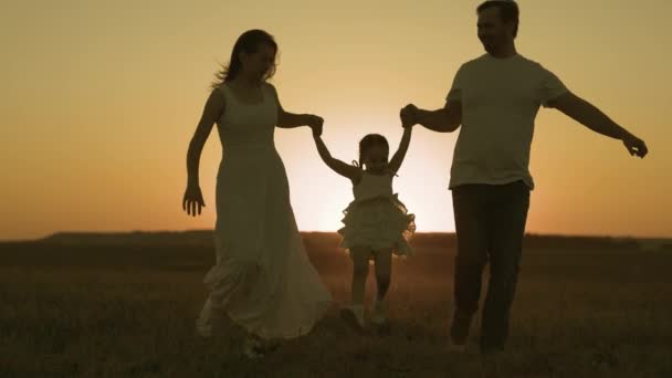 Pai feliz e mãe correm através do campo com o pôr do sol da criança pequena no céu, família alegre silhueta, sonho de infância dos pais, brincar juntos, dar atenção às crianças, amor da mãe e do pai para a criança — Vídeo de Stock