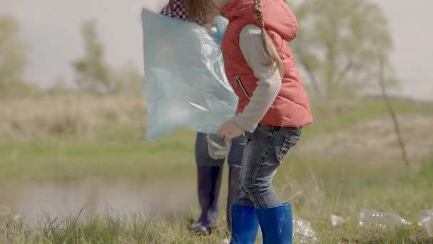Een klein kind verzamelt afval in een vrijwilliger team, een gelukkig gezin, het schoonmaken van de ecologie van de aarde uit afval, een eco-systeem, het houden van de rustplaatsen schoon, kind met zijn moeder doet schoonmaken — Stockvideo