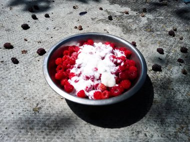 Su dolu metal bir kasede kırmızı ahududular, susuz bir kasede, kremayla dolu bir kasede şekerle serpiştirilmiş bir kasede.