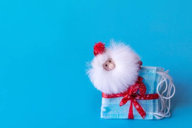 Kırmızı kurdeleli tıbbi koruyucu maskeler ve mavi arka planda Noel Baba. Yeni Yıl ve Noel konsepti.
