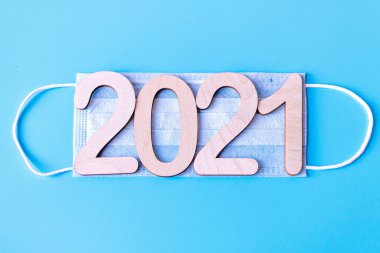 2021 numara mavi arka planda tıbbi koruyucu bir maske takıyor. Koronavirüs salgınında Noel ve Yeni Yıl kavramı.