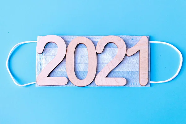 2021 numara mavi arka planda tıbbi koruyucu bir maske takıyor. Koronavirüs salgınında Noel ve Yeni Yıl kavramı.