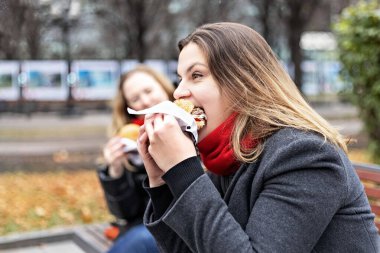 Genç, aç bir kadın hamburger yer ve öğle yemeğini dışarıda dışarıda yer. Fast food. Paket yemek konsepti.