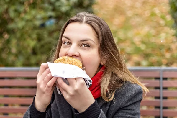 Young hungry woman eats Burger and takes lunch break outdoors in Park.Fast food. Takeaway food concept.