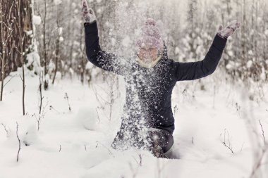 Oturan genç bir kadın kış ormanına yumuşak kar fırlatıyor..