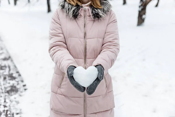 Women\'s hands in warm gray mittens with a snowy white heart. The Concept Of Valentine\'s Day.
