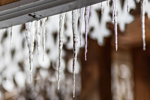 A large transparent ice icicle hangs from the roof of the house. Winter frosts.