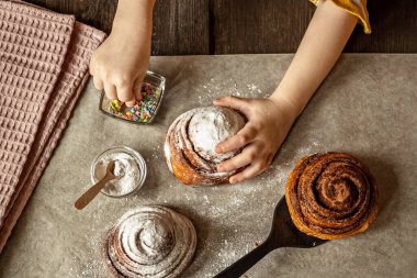 Çerçevedeki çocukların elleri üzerine taze pişmiş bir çörek serpiştirir üzerine tarçın serpiştirir..