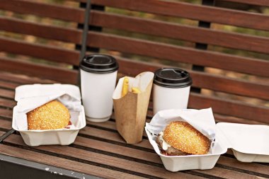 Fast food. Kahve bardakları, hamburger kutuları ve kızartmalar park bankında. Paket yemek kavramı..