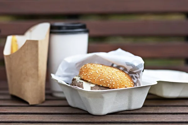 Fast food. Paper cups with coffee, hamburger boxes and fries on a park bench.Takeaway food concept.