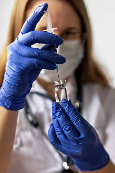 A female doctor wearing a medical mask draws the coronavirus vaccine into a syringe at the clinic.The concept of vaccination, immunization, prevention against Covid-19