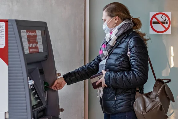 Yüzüne koruyucu tıbbi maske takmış bir kadın kredi kartı takıyor ve ATM 'den para çekiyor.