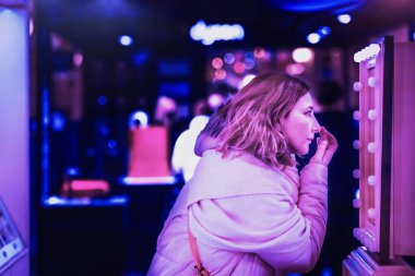 Aynanın önünde duran genç bir kadın makyajını yüzüne yapıyor..