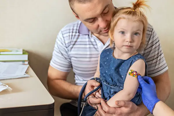 A little girl with her father in the doctor\'s office at the clinic is being vaccinated against the coronavirus.The concept of vaccination, immunization, prevention against Covid-19