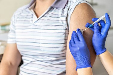 Bir doktor, klinikte bir adamı koronavirüse karşı aşılıyor. Yakın plan. Covid-19 'a karşı aşı, aşı, aşı, önleme kavramı