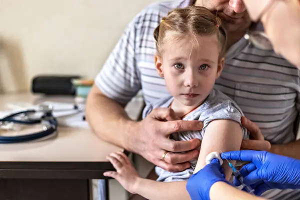 A little girl with her father in the doctor\'s office at the clinic is being vaccinated against the coronavirus. The concept of vaccination, immunization, prevention against Covid-19