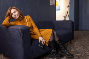 Kızıl saçlı, gülümseyen bir kadının portresi. Kafasını kanepenin arkasında dinlendiriyor..