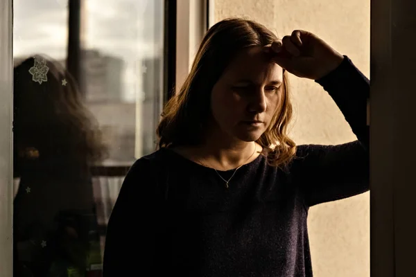 Portrait of a young woman at the window at sunset.