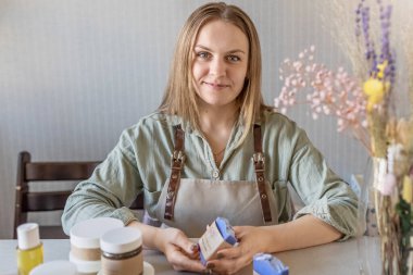 Bir kadın sabun üreticisi yeni hazırlanmış el yapımı sabunları ve vücut bakım ürünlerini paketler. Emirleri bir araya getirme süreci. Ev spası. Küçük işletme