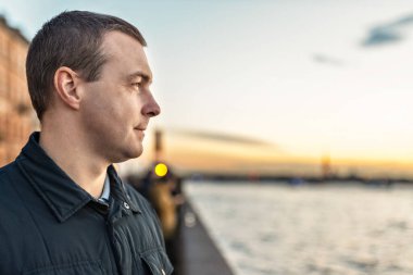 Nehrin kenarında gün batımını izleyen genç bir adamın portresi..