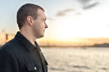 Nehrin kenarında gün batımını izleyen genç bir adamın portresi..