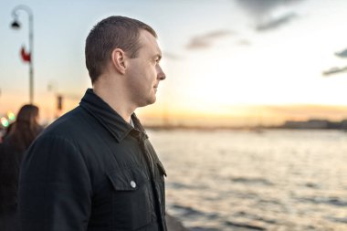 Nehrin kenarında gün batımını izleyen genç bir adamın portresi..