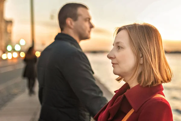 stock image Young couple man and woman on the embankment of the river in the city. Look in different directions, quarrel.Sunset.