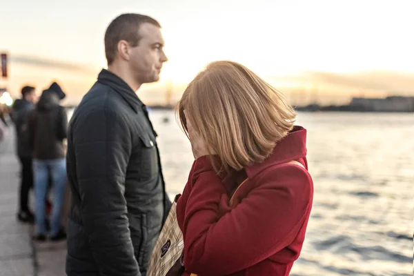 Young couple man and woman in a quarrel, on the embankment of the river in the city at sunset. The girl covered her face with her hands, crying. Emotions.