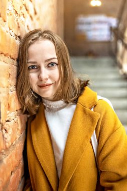 Parlak sarı ceketli genç bir kadının portresi pencere kenarındaki tuğla duvarın arkasında. Gün ışığında.