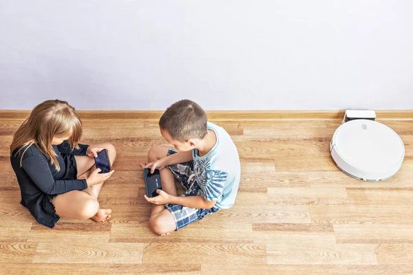 Bir erkek ve bir kız çocuğu yerde oturuyorlar, birbirlerinin karşısında. Akıllı telefonlarıyla online oyun oynuyorlar. Gen Z, Aile, Telefon, Kullanım, Cep Telefonu. Üst görünüm.