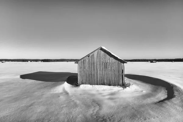 The winter sun creates strong shadows on the snowy fields. The old barn house stands alone on the vast fields.