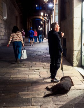 İspanya 'nın eski Barselona kasabasında bir adam saatine bakıyor. Köpeği şimdiden ayaklarının dibinde uyuyor..