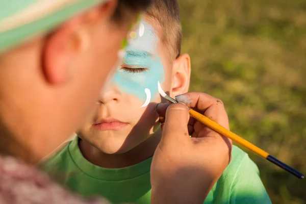 Vrouw doet greasepaint op gezicht van het kind — Stockfoto